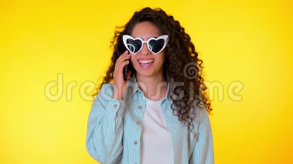 年轻女性微笑着在手机上用黄色背景说话漂亮的混血女孩抱着视频的预览图