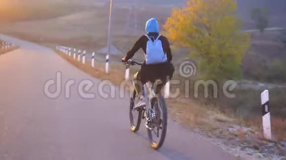 穆斯林妇女戴着头巾背着背包骑着自行车快速上路美丽的日落后景视频的预览图