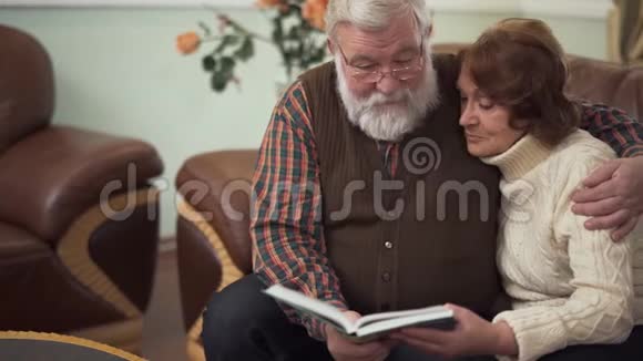 一对老夫妇看着一本大书或一张专辑愉快地交谈怀旧和欢笑视频的预览图