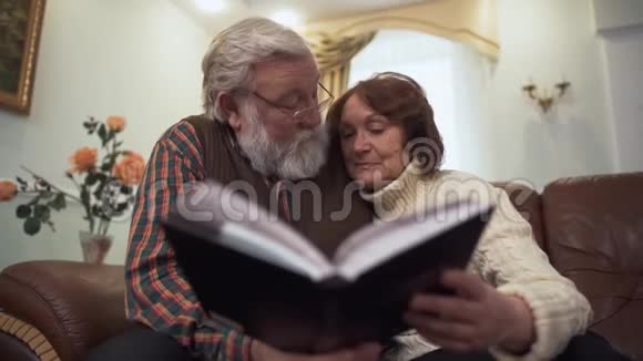 一对成熟的夫妇看着一本大书或一张专辑愉快地交谈怀旧和欢笑视频的预览图