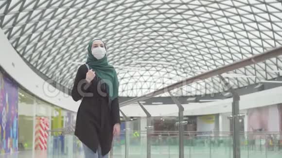 戴着头巾背着背包脸上戴着医疗面具的漂亮穆斯林女人去购物慢条斯理视频的预览图