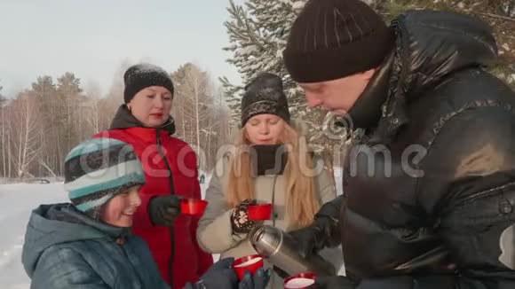 父亲从保温瓶里倒热茶给家人冬天在森林散步视频的预览图
