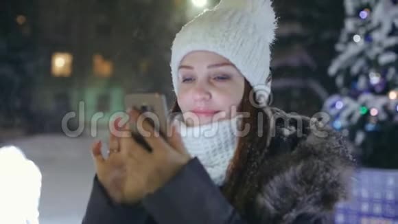 一位女士在圣诞树附近的广场上戴着智能手机在社交网络上分享照片视频的预览图