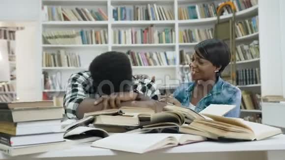 疲惫的非洲年轻人睡在书上而非洲年轻的女人在现代图书馆叫醒他视频的预览图