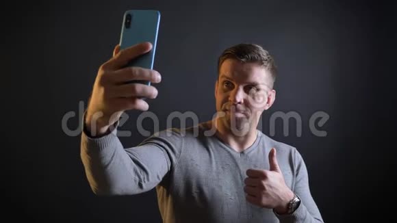 中年白种人用智能手机在黑色背景下制作自拍照片的特写肖像视频的预览图