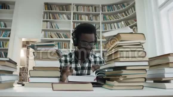 微笑着非洲男学生一边读书一边用耳机听音乐视频的预览图