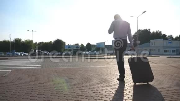 商人带着行李从机场到出租车停车场打电话在户外散步的年轻人视频的预览图