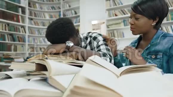 非洲女学生看书而疲惫的非洲男学生睡在书上叫醒他视频的预览图