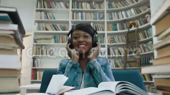 非洲迷人的年轻女子坐在书旁听音乐的肖像视频的预览图