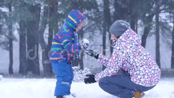 在一个美丽的冬天下雪的一天妈妈和儿子在外面的森林或公园里玩得很开心一个孩子扔了视频的预览图