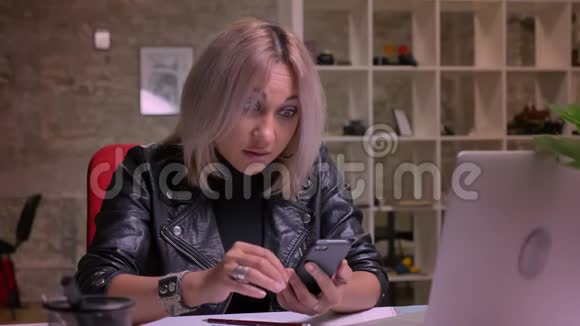 一个漂亮的白种人女人坐在室内的时候正看着手机和屏幕视频的预览图