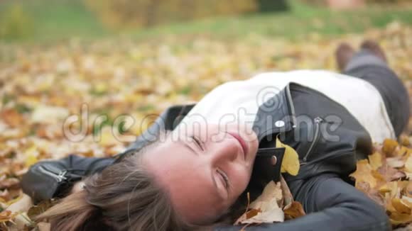一个美丽的年轻女子躺在树下的黄色叶子上视频的预览图