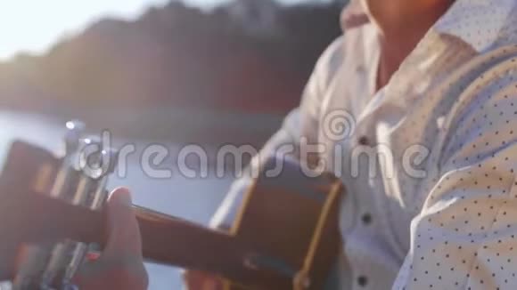 人弹吉他对着湖面唱歌吉他手触摸吉他弦近距离射击视频的预览图