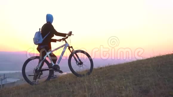 穆斯林妇女戴着头巾背着一个背包骑着自行车上坡看日落慢悠悠视频的预览图