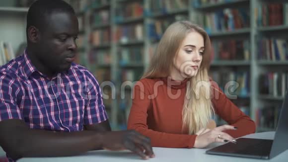 白种人女士和美国黑人男子在图书馆学习视频的预览图