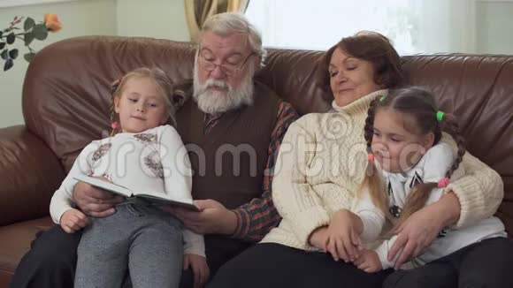 祖父和祖母坐在现代客厅的皮革沙发上附近有两个小女孩成年男子读书视频的预览图