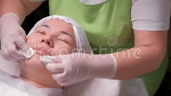 穿绿色连衣裙的美容师用棉垫擦拭东方女孩的脸一位在美容院的亚洲穆斯林妇女撒谎视频的预览图