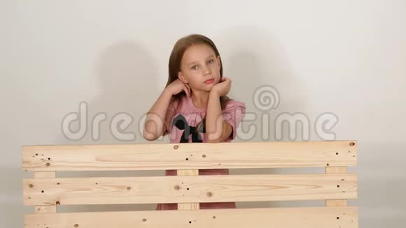 可爱的女婴站在一个白色墙壁的房间里靠在一张木凳上视频的预览图
