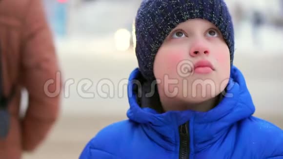 穿着蓝色羽绒服的少年站在街上汽车在后台行驶男孩环顾四周视频的预览图