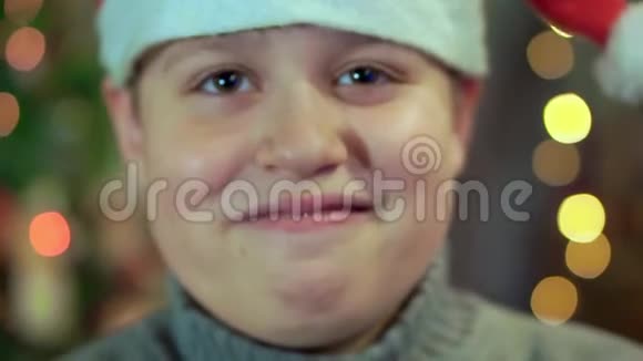 穿着毛衣和圣诞老人帽子的男孩笑了特写背景是圣诞灯视频的预览图