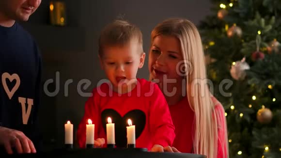 新年圣诞节男孩和父母在圣诞树旁边的壁炉旁看着燃烧的东西视频的预览图