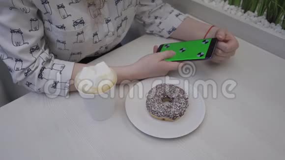 特写一名年轻女子手里拿着手机绿屏桌子上有一个甜甜圈和咖啡视频的预览图
