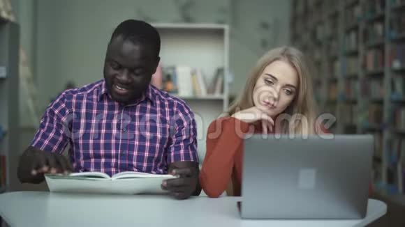 可爱的疲惫的女孩带着笔记本电脑她的非裔美国朋友在看书视频的预览图
