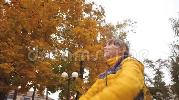 快乐的女孩在秋天的公园里扔黄叶微笑着慢动作秋天在公园休息的小女孩视频的预览图