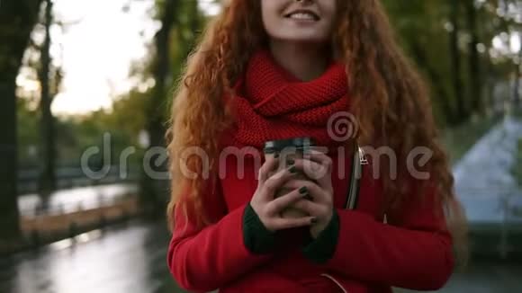 美丽兴奋的年轻女子穿着红色外套在一个多雨的秋天带着外卖饮料在街上散步年轻貌美视频的预览图