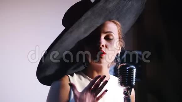 一个戴着黑色优雅大帽子的女人站在麦克风和情绪化的歌声后面视频的预览图