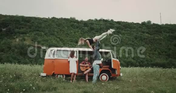 在大自然为一群朋友跳舞弹吉他坐在复古的面包车上4k视频的预览图