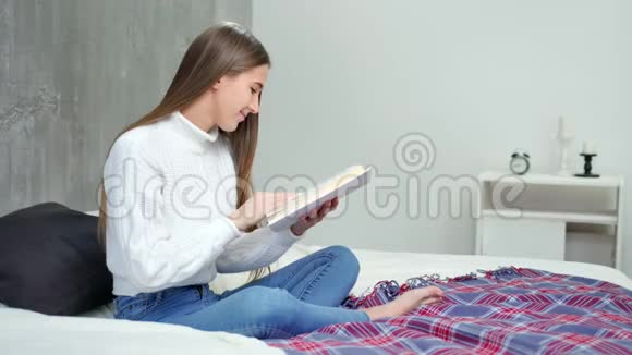 摘要年轻女学生阅读教科书并在家中的床上微笑全镜头视频的预览图