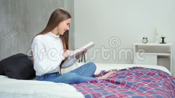热情的年轻女孩在家舒适的卧室里读有趣的书视频的预览图