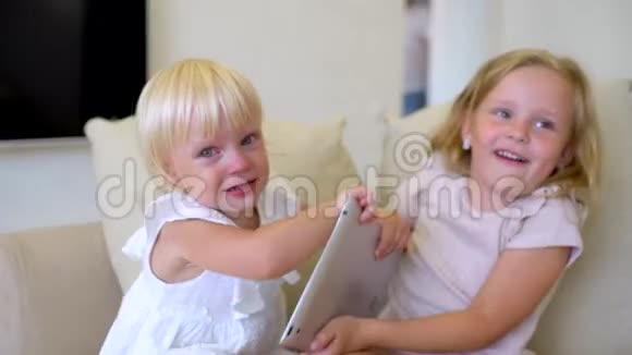 两个孩子在家用平板电脑看ang儿童使用现代笔记本电脑平板电脑在沙发上姐妹们为争吵视频的预览图