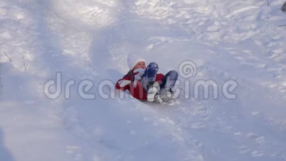 快乐的孩子滑在雪上滑在雪橇上挥动他的手小女孩正在公园里玩冬天的游戏视频的预览图