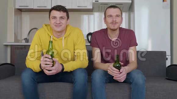 两个人坐在沙发上看电视上的足球赛喝啤酒评论和微笑视频的预览图