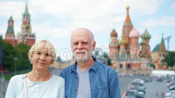 这对老夫妇站在俄罗斯莫斯科圣巴西尔大教堂和克里姆林宫钟楼的背景下视频的预览图