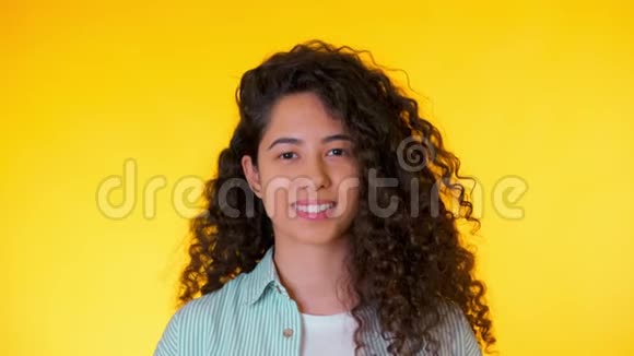 西班牙裔年轻学生女孩的肖像黄色背景上有卷发时髦可爱的女人对着镜头微笑工作室视频的预览图
