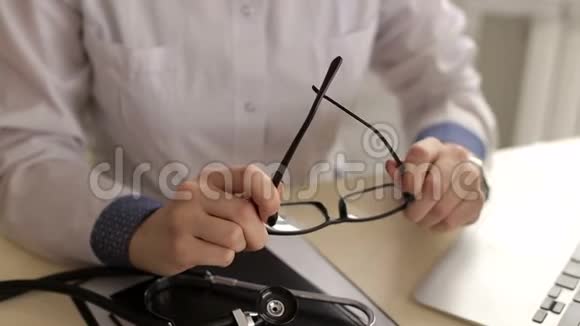 一名女医生拿着眼镜坐在医院的办公桌前的特写镜头视频的预览图