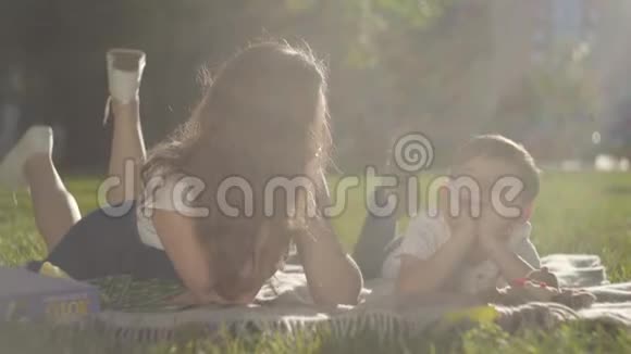 户外姐姐和弟弟的肖像那个男孩和女孩一起躺在公园的草地上夏季视频的预览图