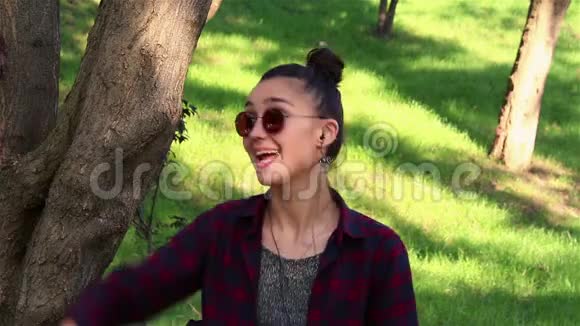 戴着太阳镜的漂亮女孩积极地笑着在公园里坐在长凳上时竖起大拇指视频的预览图