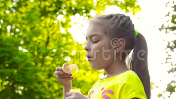 公园里穿黄色t恤吹肥皂泡的小女孩视频的预览图