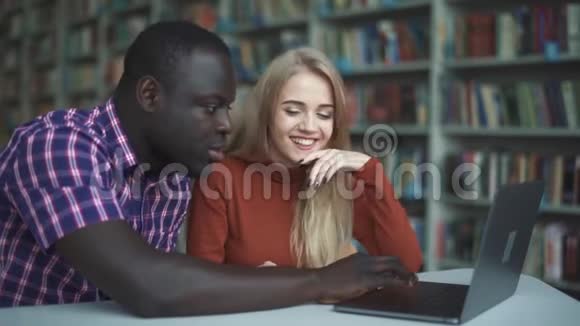 一位欧洲女士和一位非洲裔美国人在用笔记本电脑工作时笑了视频的预览图