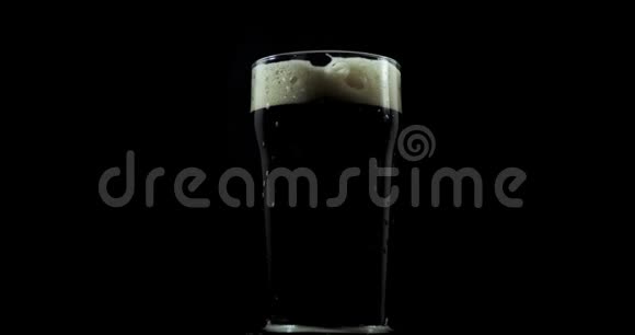 在一家私人啤酒厂为节日制作的深色工艺啤酒被倒入一个在黑色背景上旋转的玻璃杯中视频的预览图
