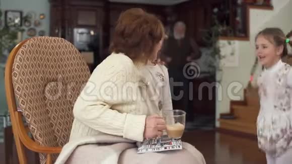 坐在摇椅上的成熟女人和她可爱的小孙女来到她身边亲吻并轻轻拥抱视频的预览图