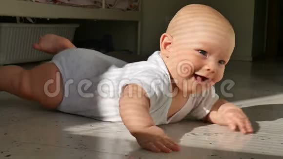 一个可爱的半岁婴儿躺在地板上兴高采烈地笑着孩子敲着地板上的一条小溪视频的预览图