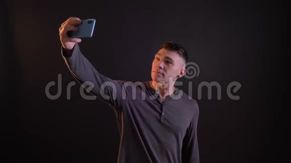 在电话里用黑色背景做自拍的英俊白种人的特写镜头视频的预览图