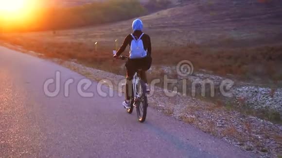 穆斯林妇女戴着头巾背着背包骑着自行车在路上夕阳西下后景慢悠悠视频的预览图
