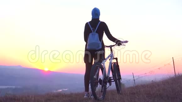 穆斯林妇女戴着头巾背着一个背包骑着自行车看着夕阳高兴地举起双手慢悠悠地说视频的预览图