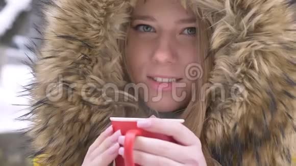 在冬天的街道上一幅美丽的年轻白种人女孩的特写肖像她喝着一杯热饮料微笑着对着镜头视频的预览图